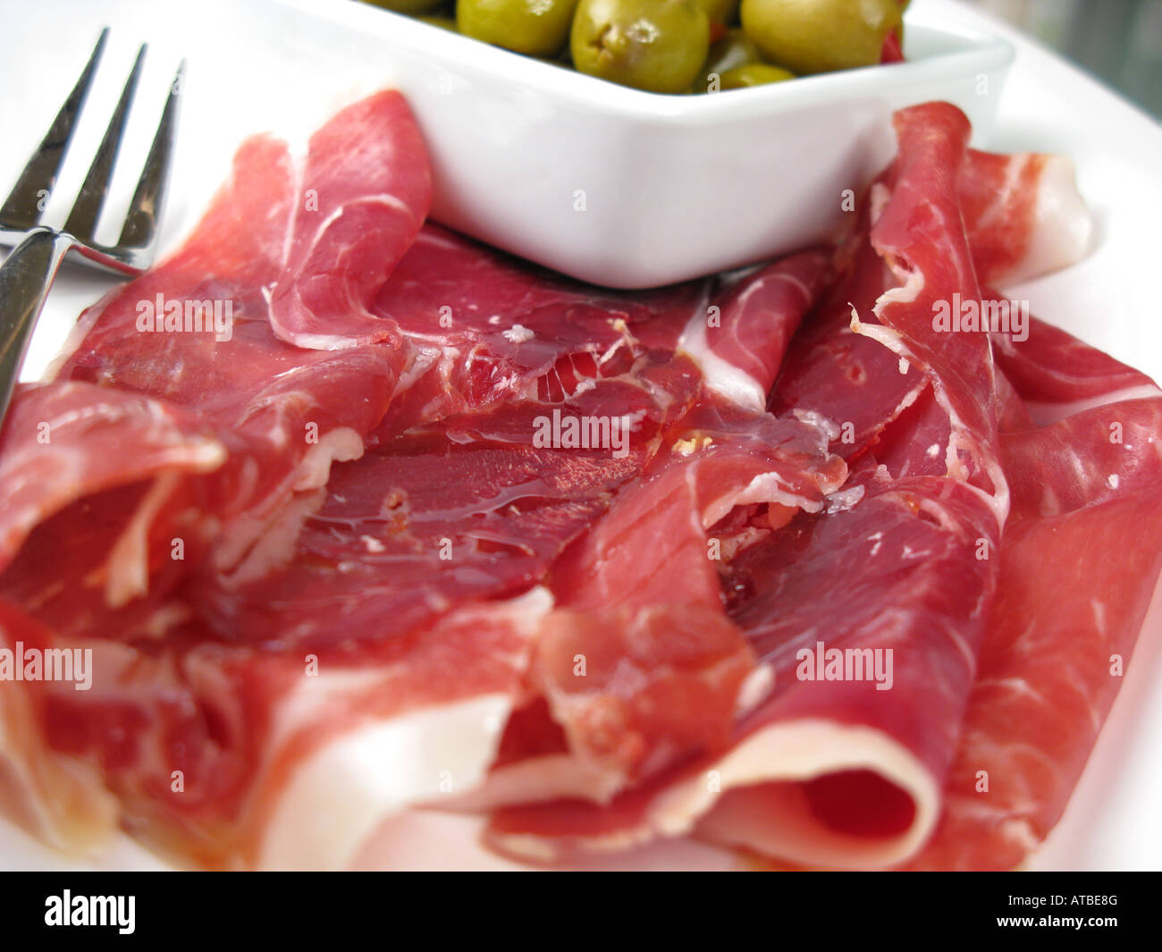 Spanish style tapas of thinly-sliced Jamon Iberico de Bellota with pepper-stuffed olives. Stock Photo