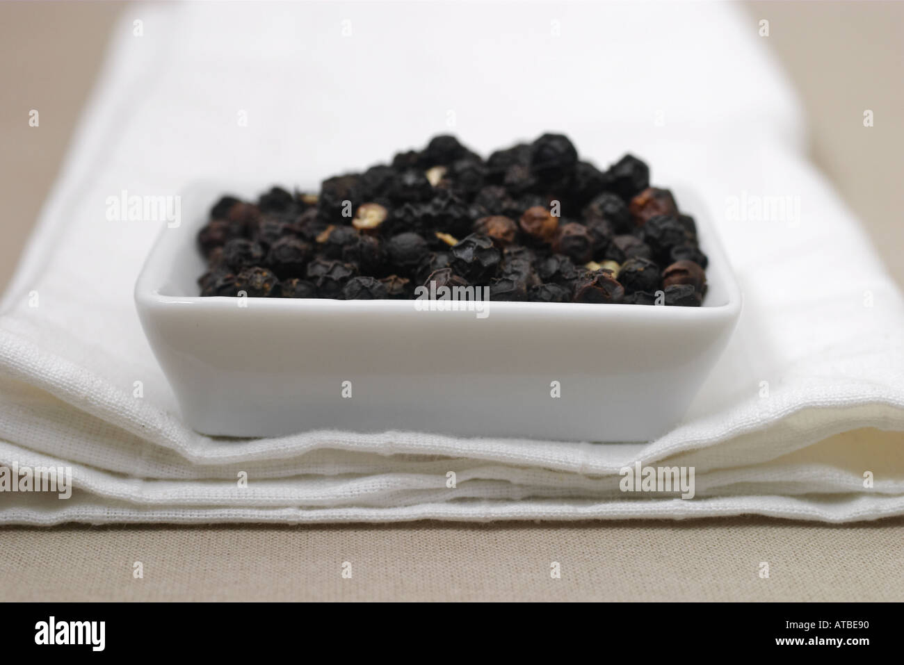Black pepper in white bowl on white napkin Stock Photo