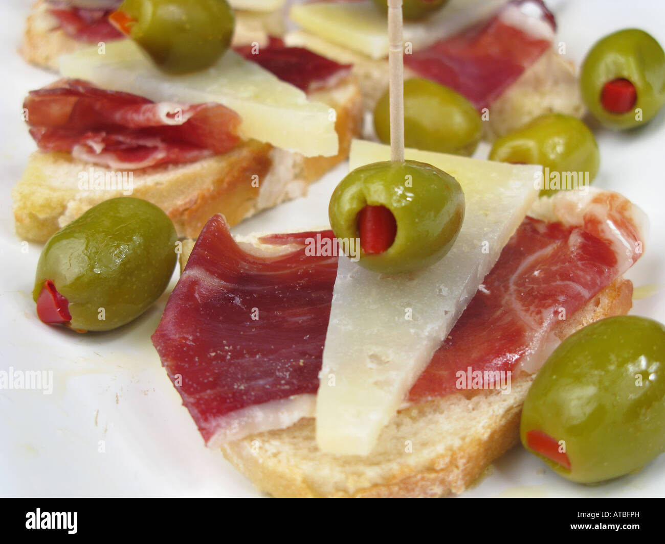 Spanish style tapa of sliced Jamon Iberico de Bellota and Manchego cheese with pepper stuffed olives on crusty stonebaked bread. Stock Photo