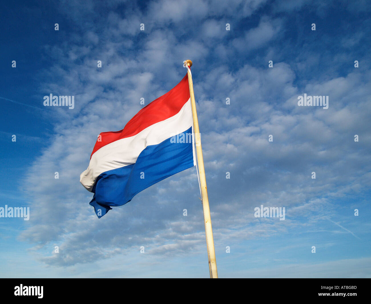 Dutch flag on a pole waving in the wind with blue sky and clouds as background Stock Photo