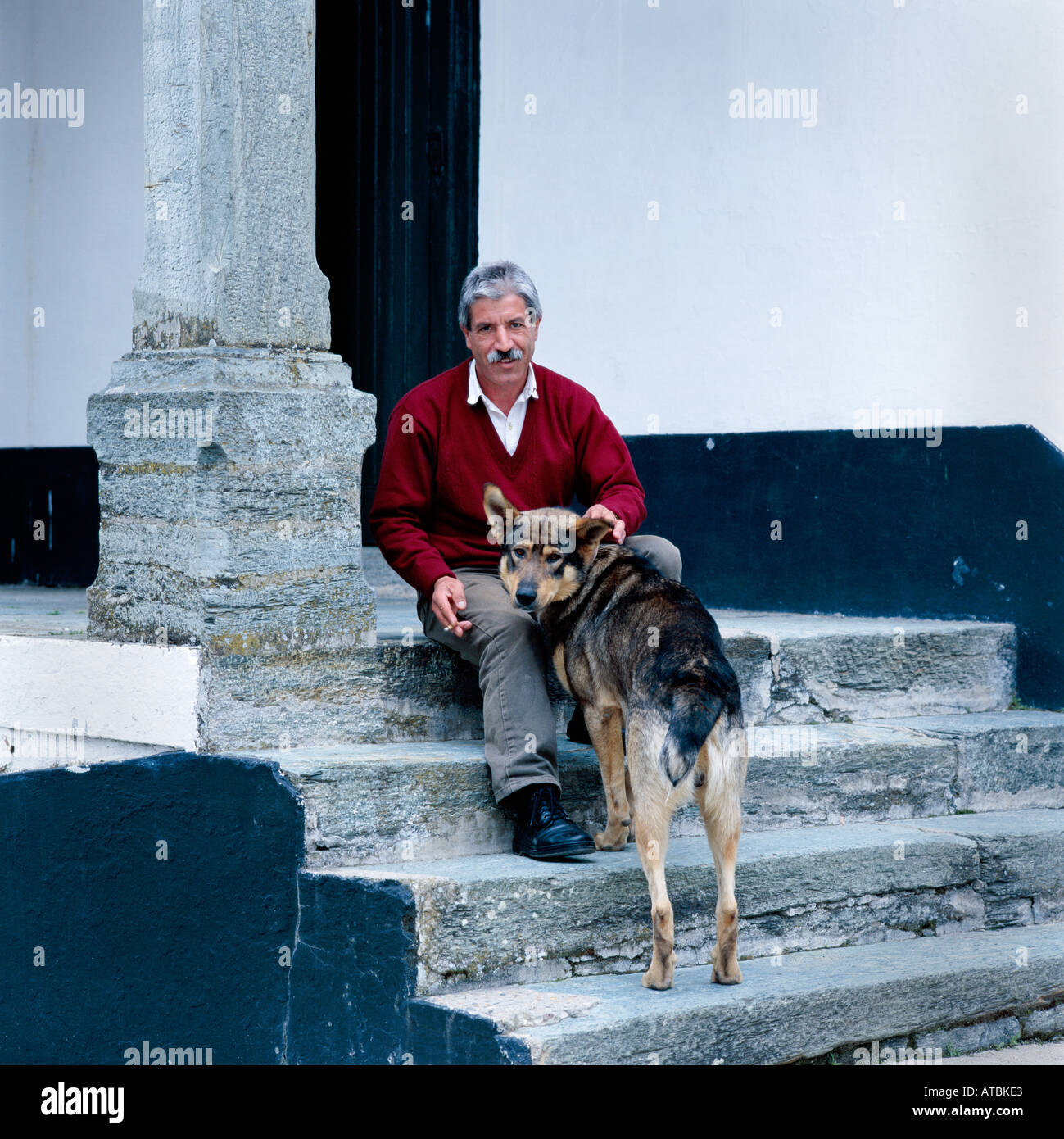 middle aged man in portugal sitting on a step with an alsatian dog Stock Photo