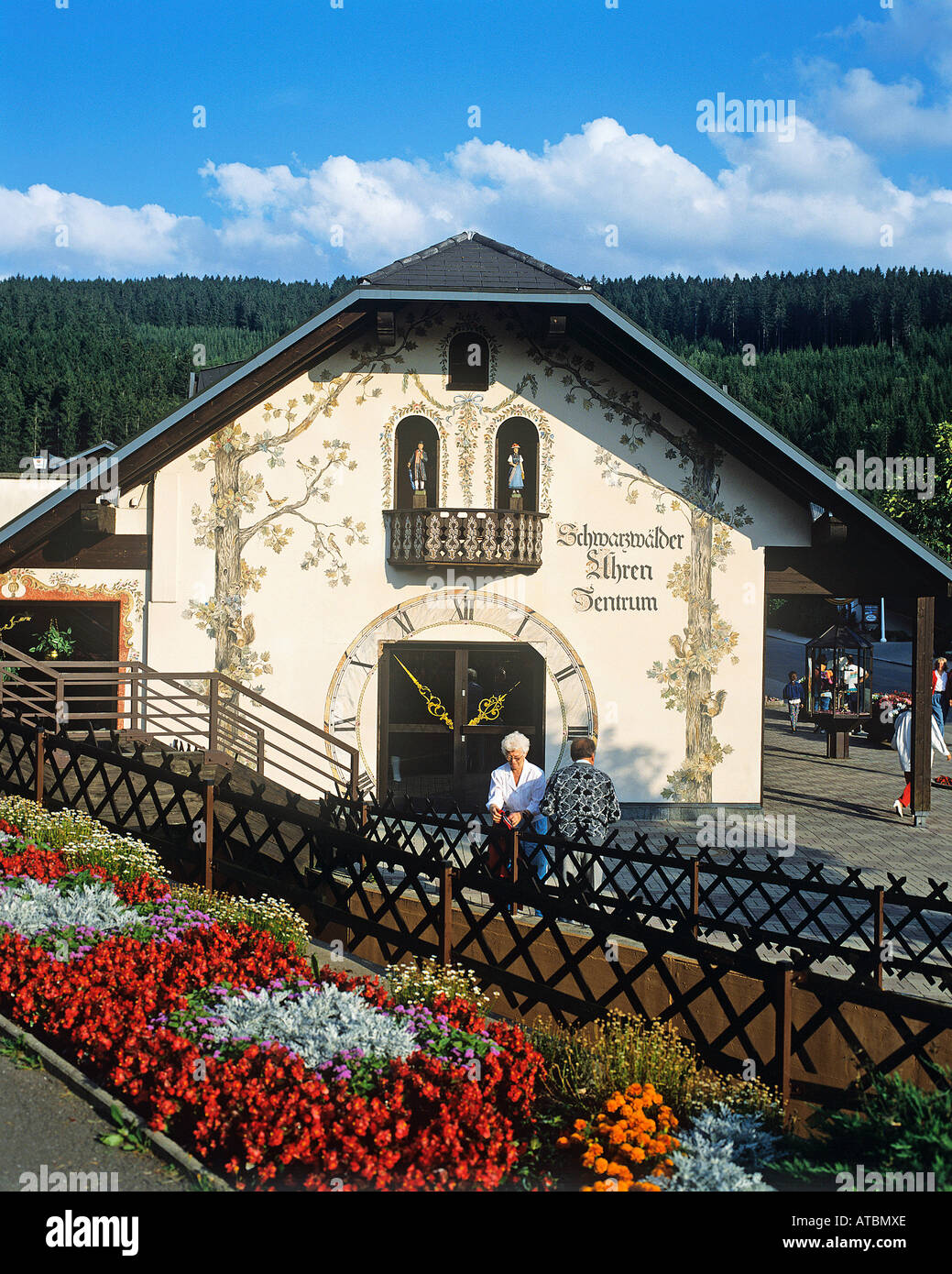 A couple standing beneath a bank of flowers outside a chalet its entire gable forming a huge cuckoo clock in the town of Titisee at the heart of the Schwarzwald Black Forest region in southwestern Germany Stock Photo