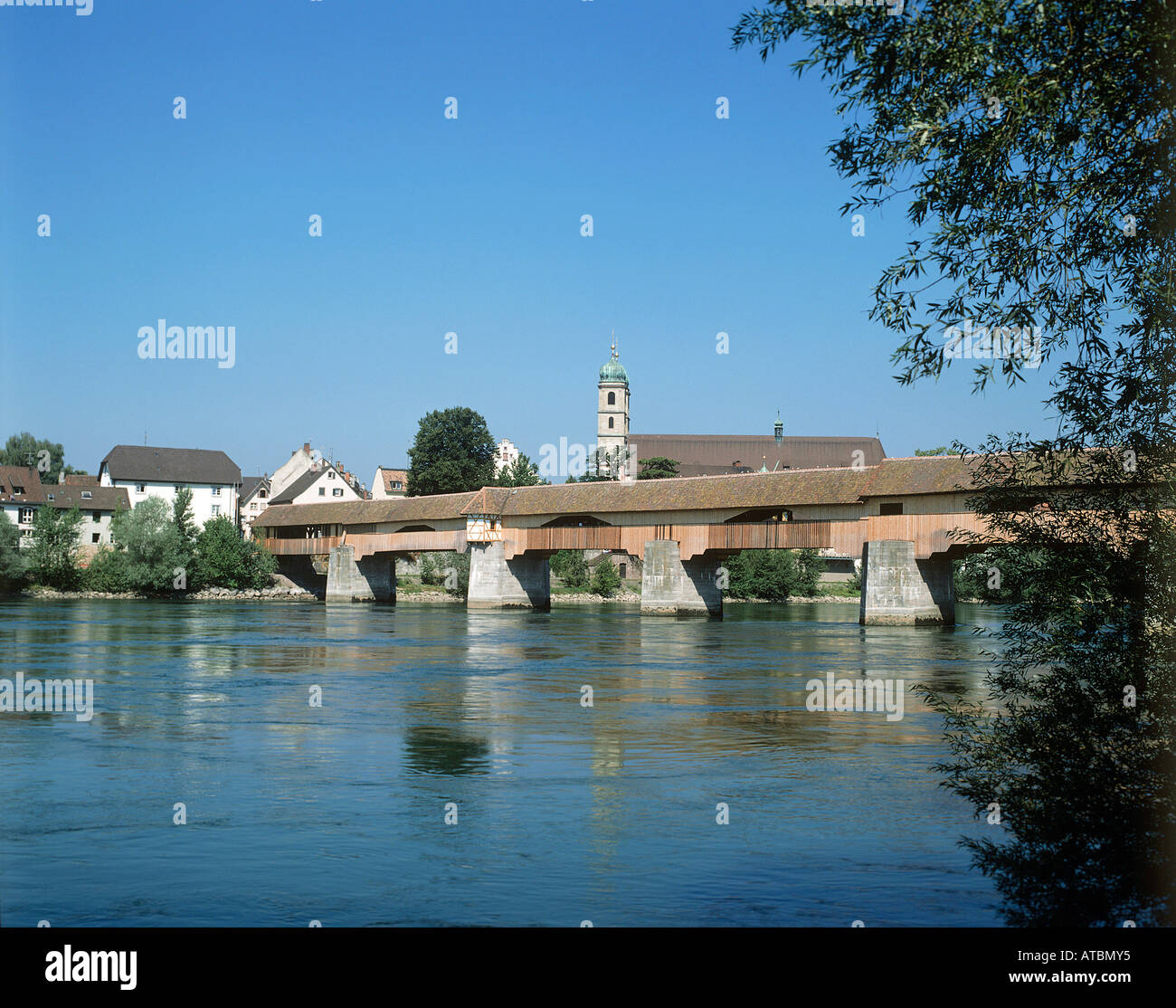 A tall church tower just visible across the old wooden bridge crossing the wide river Rhine at the health resort of Bad Sackingen in southwestern Germany Stock Photo