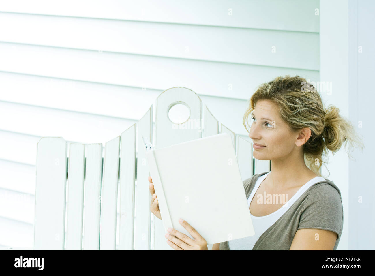 Woman sitting on bench, holding book, looking away Stock Photo