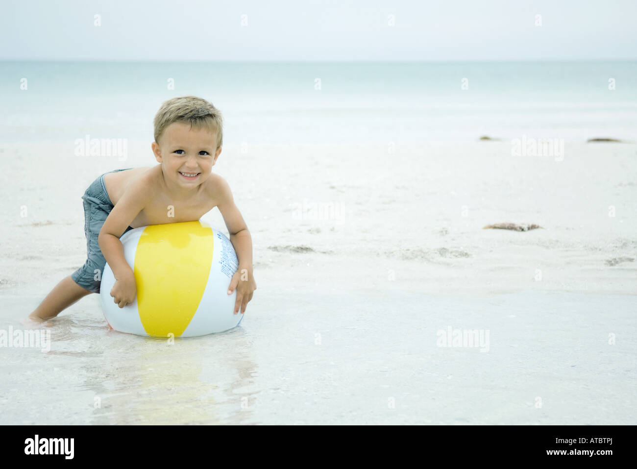 A seven year old boy playing on the beach in the sand 