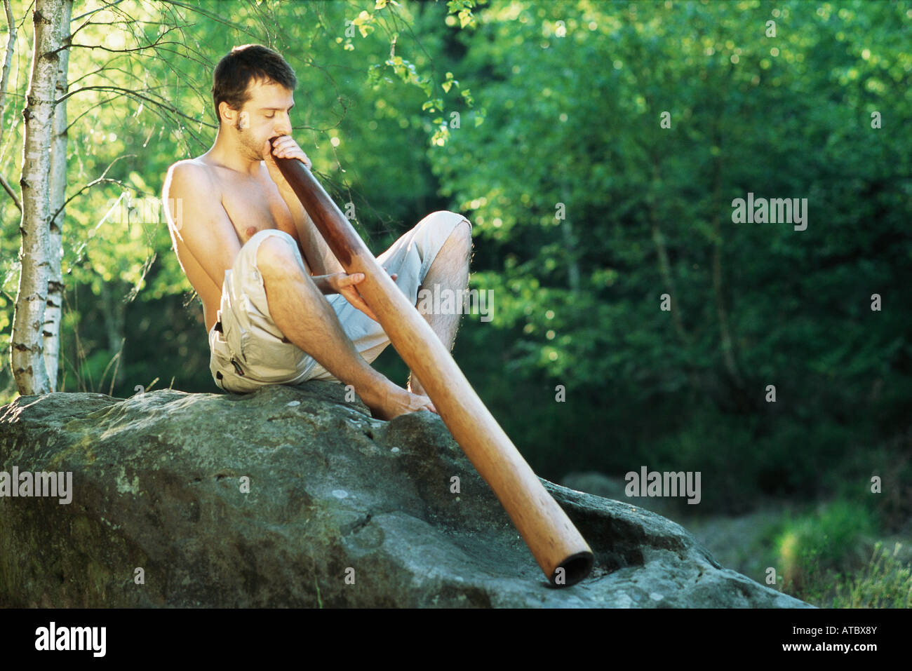 Man sitting outdoors, playing didgeridoo, eyes closed Stock Photo Alamy