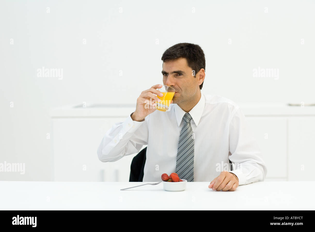 Businessman sitting at table, drinking orange juice, looking away Stock Photo