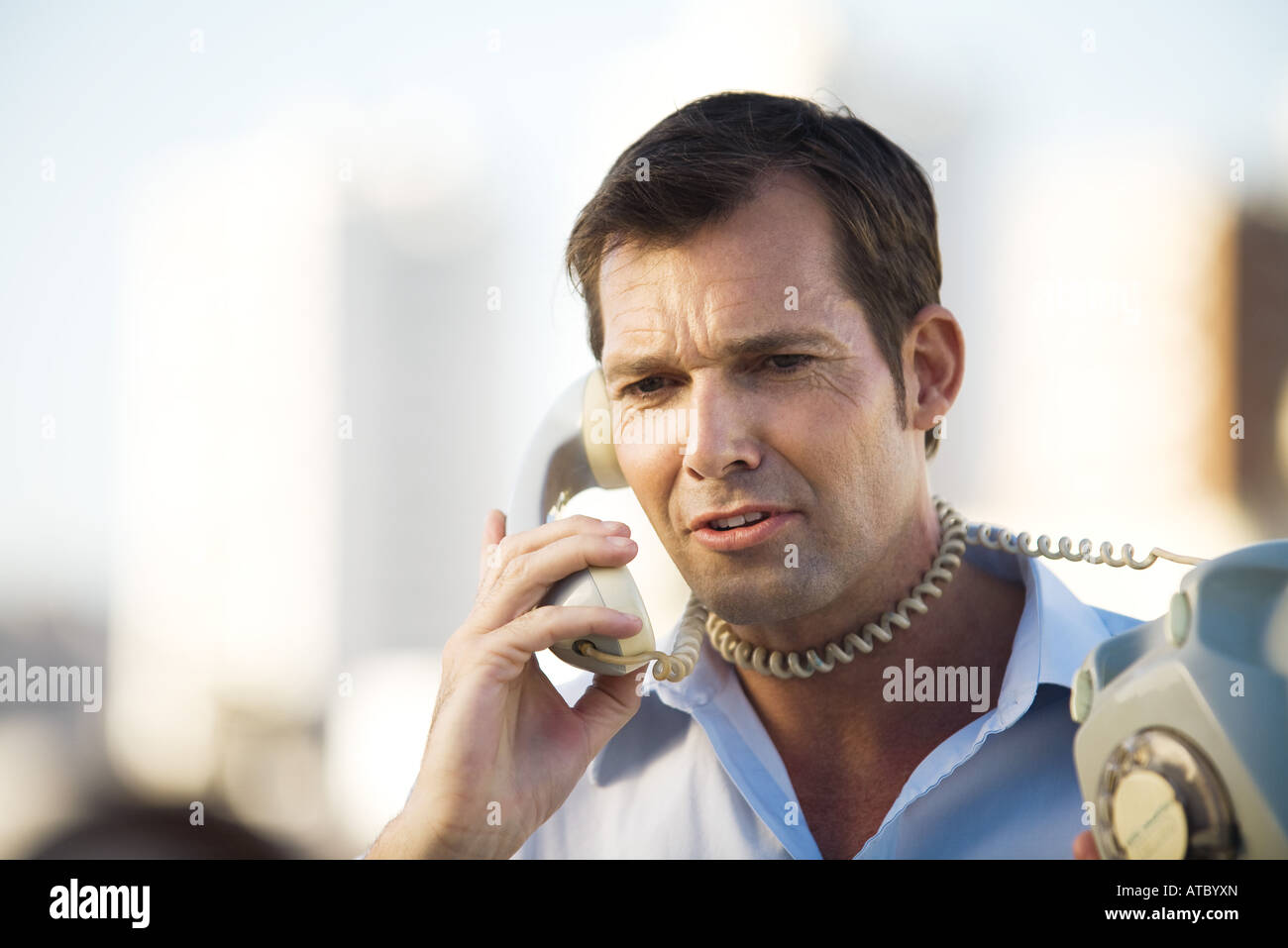 Man talking on landline phone, cord wrapped around his neck, close-up Stock Photo