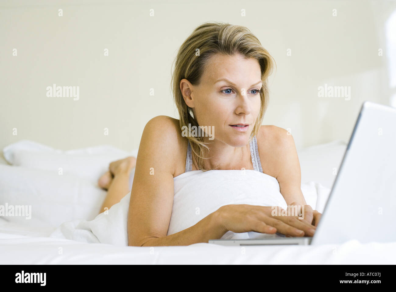 Woman lying on bed, using laptop computer, looking away Stock Photo Alamy