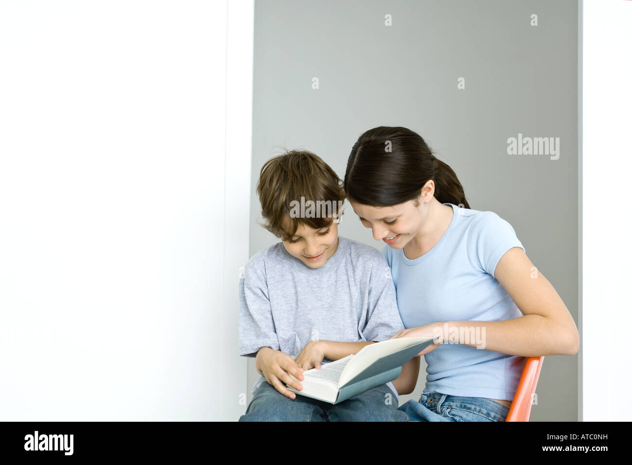 Brother and sister sitting, reading book together, both smiling Stock Photo