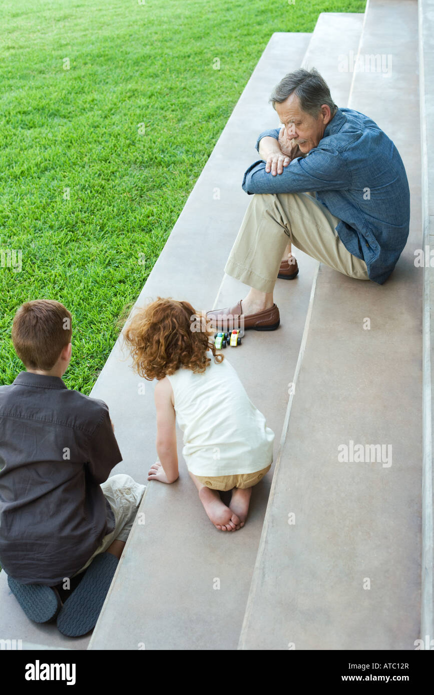 Grandfather and two grandchildren playing with toy cars together on stairs, high angle view Stock Photo
