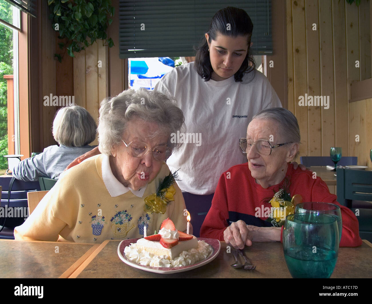 90 year old woman blows out birthday candle on cake as 88 year old partner and mid 30 year old