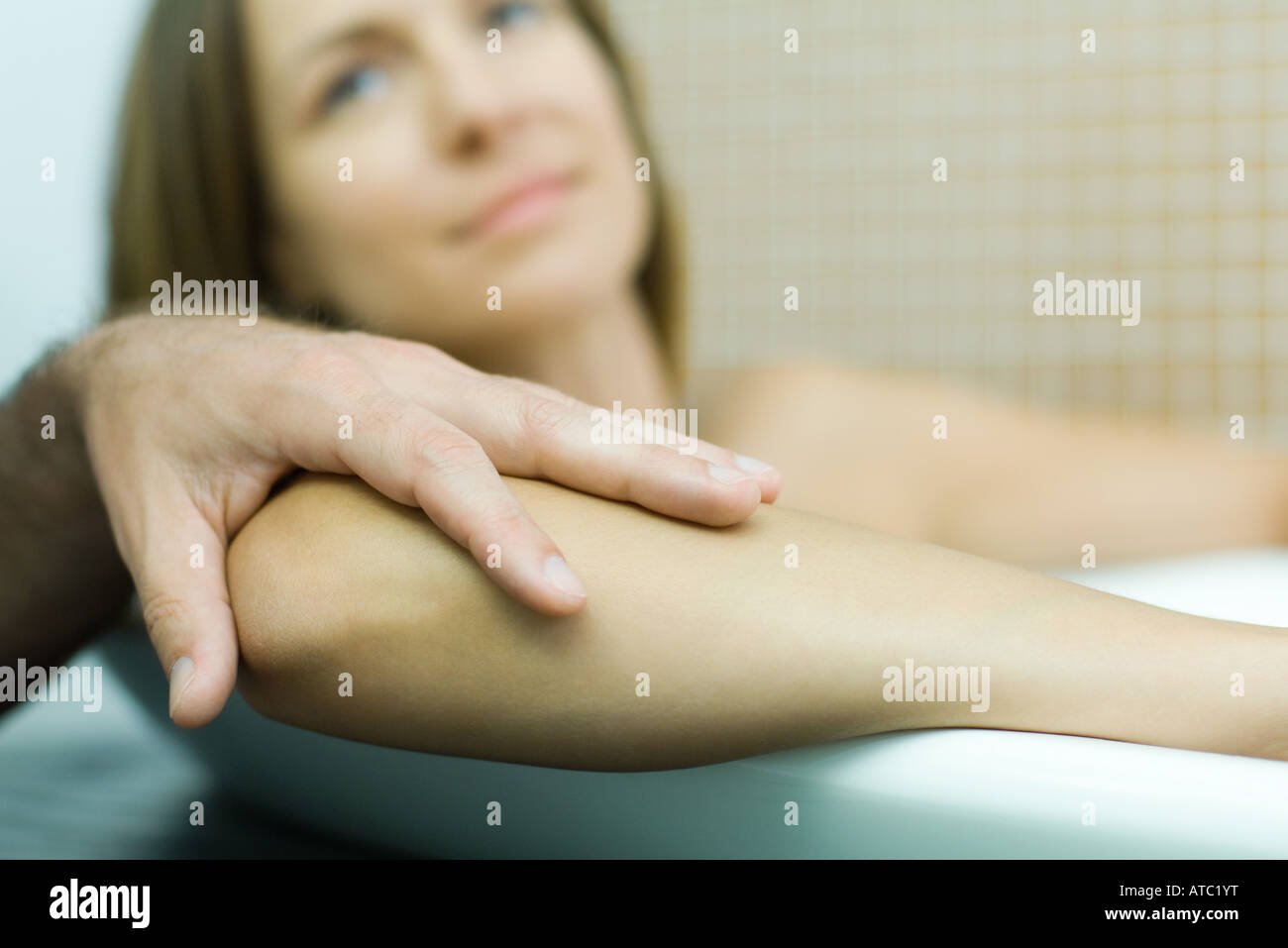 Woman in bathtub with man's hand on her elbow, focus on foreground, cropped view Stock Photo