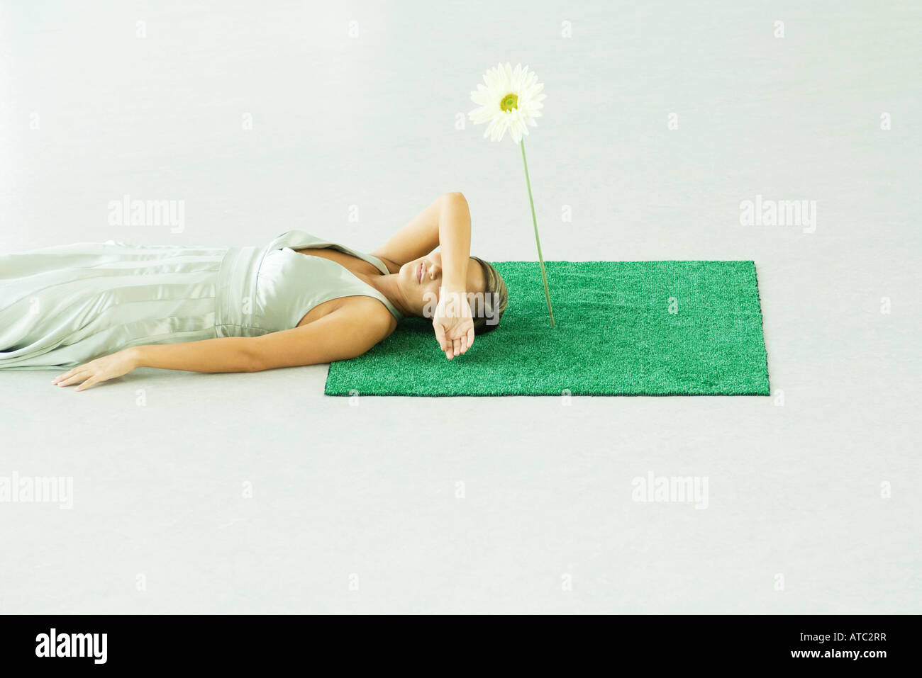 Woman lying with head on square of artificial turf, covering eyes with arm Stock Photo