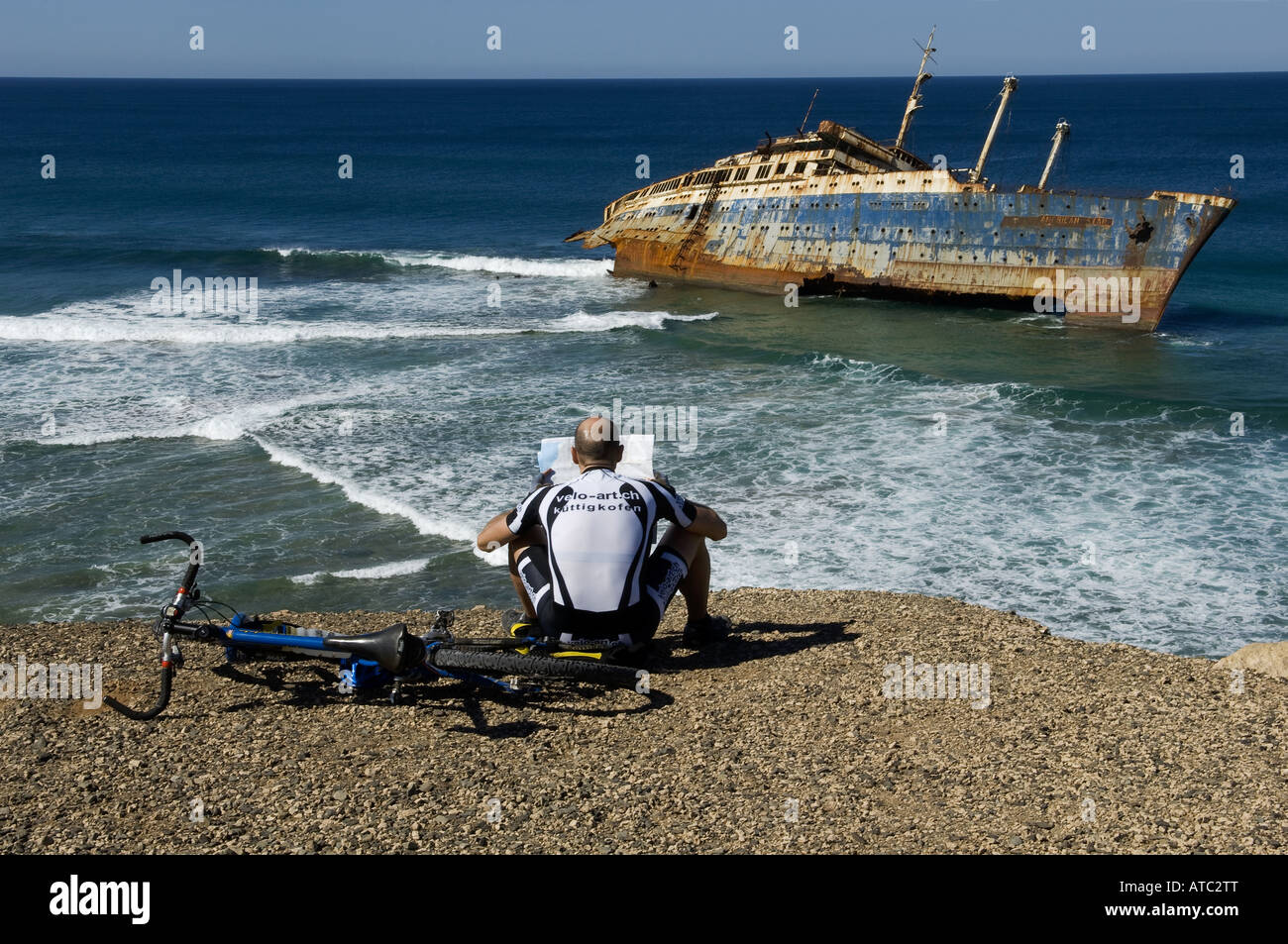 bicyclist sitting by the boat wreck of the American star in Fuerteventura Spain reading a map by the sea. Stock Photo
