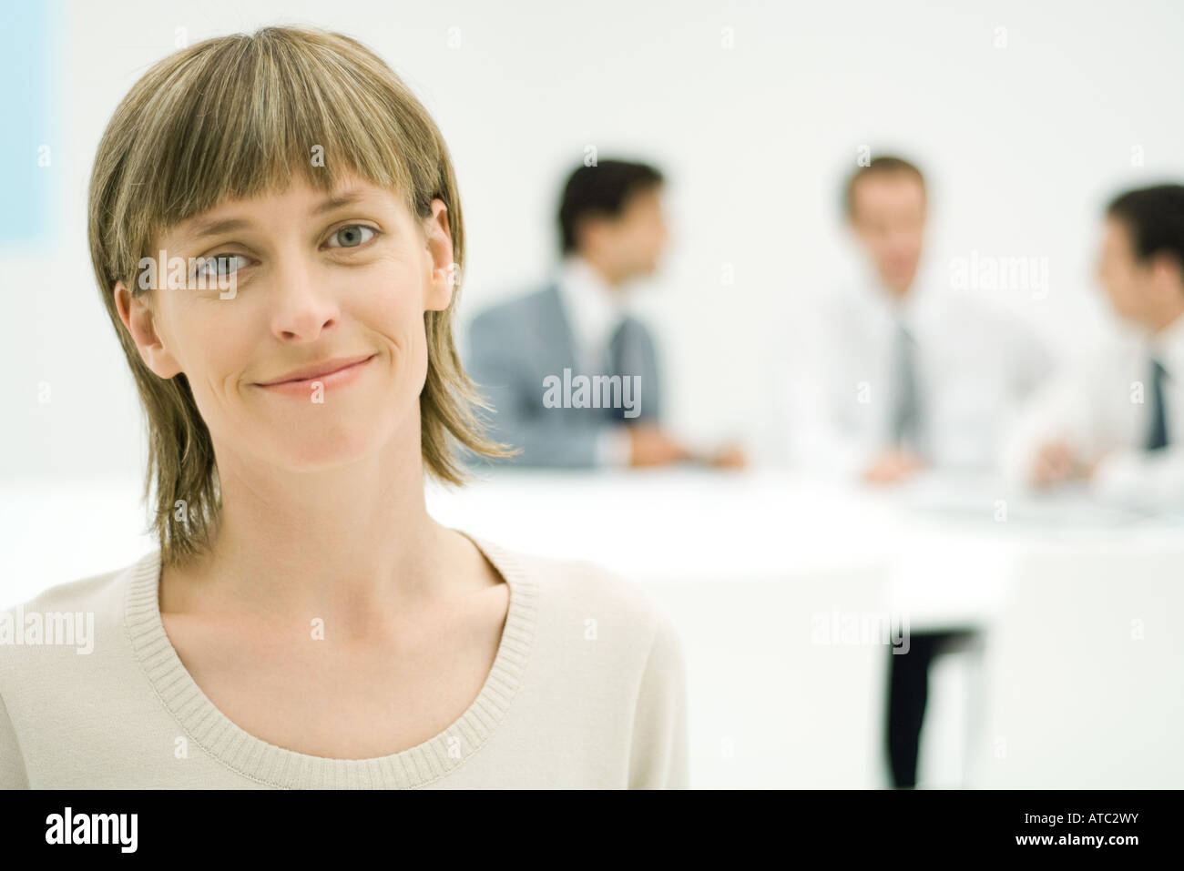 Businesswoman smiling at camera, portrait, businessmen in background Stock Photo