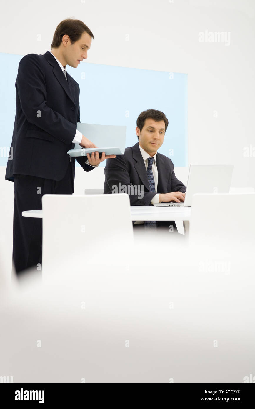Two businessmen looking at laptop computer together, one holding folder Stock Photo