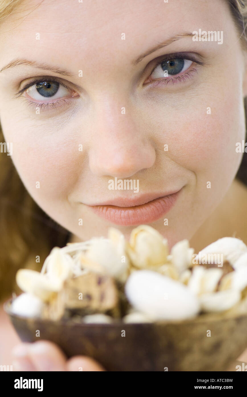 Woman holding up bowl of flowers, smiling at camera, close-up Stock Photo