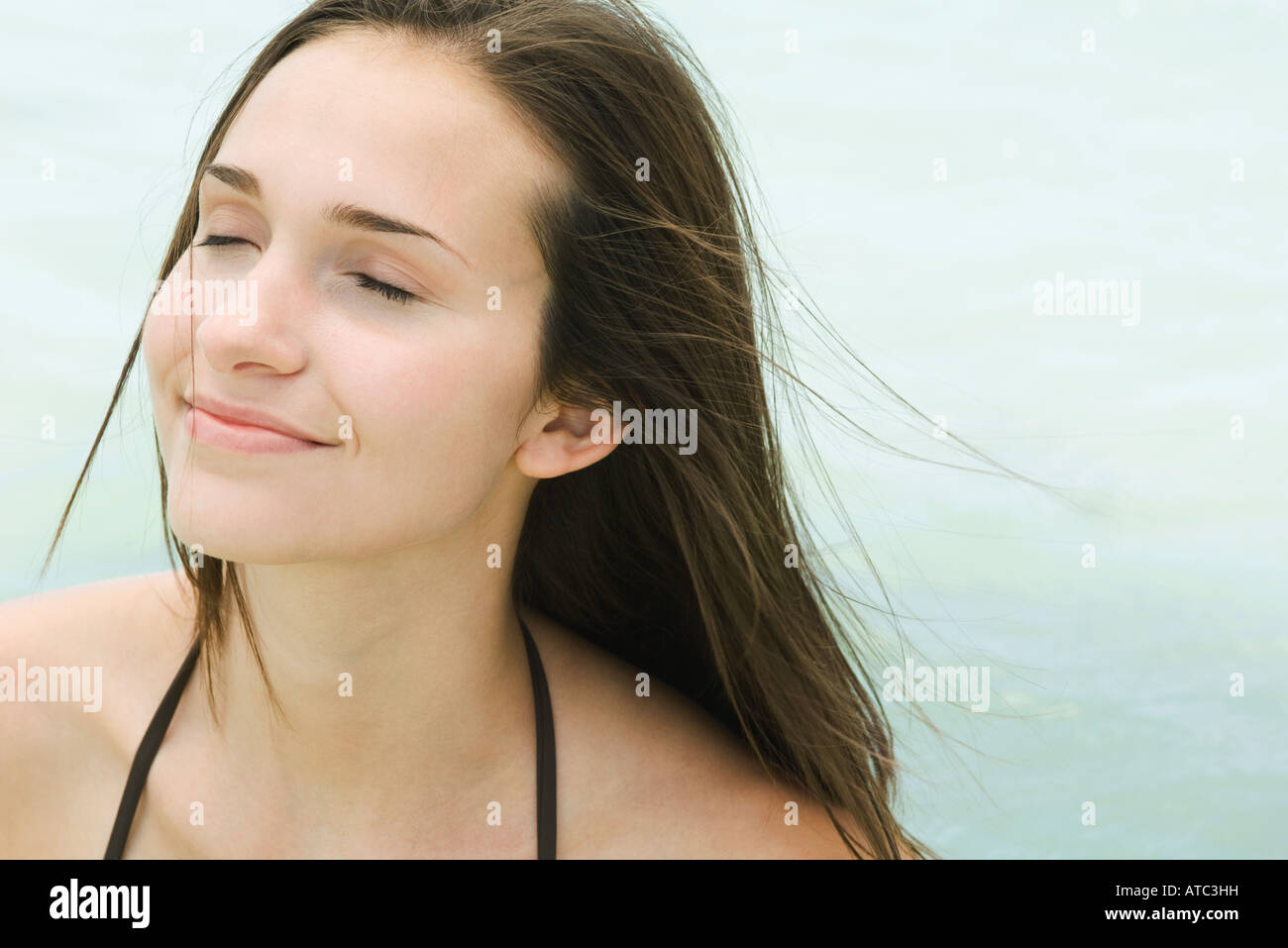 Young woman outdoors with eyes closed, hair tousled by breeze, close-up Stock Photo