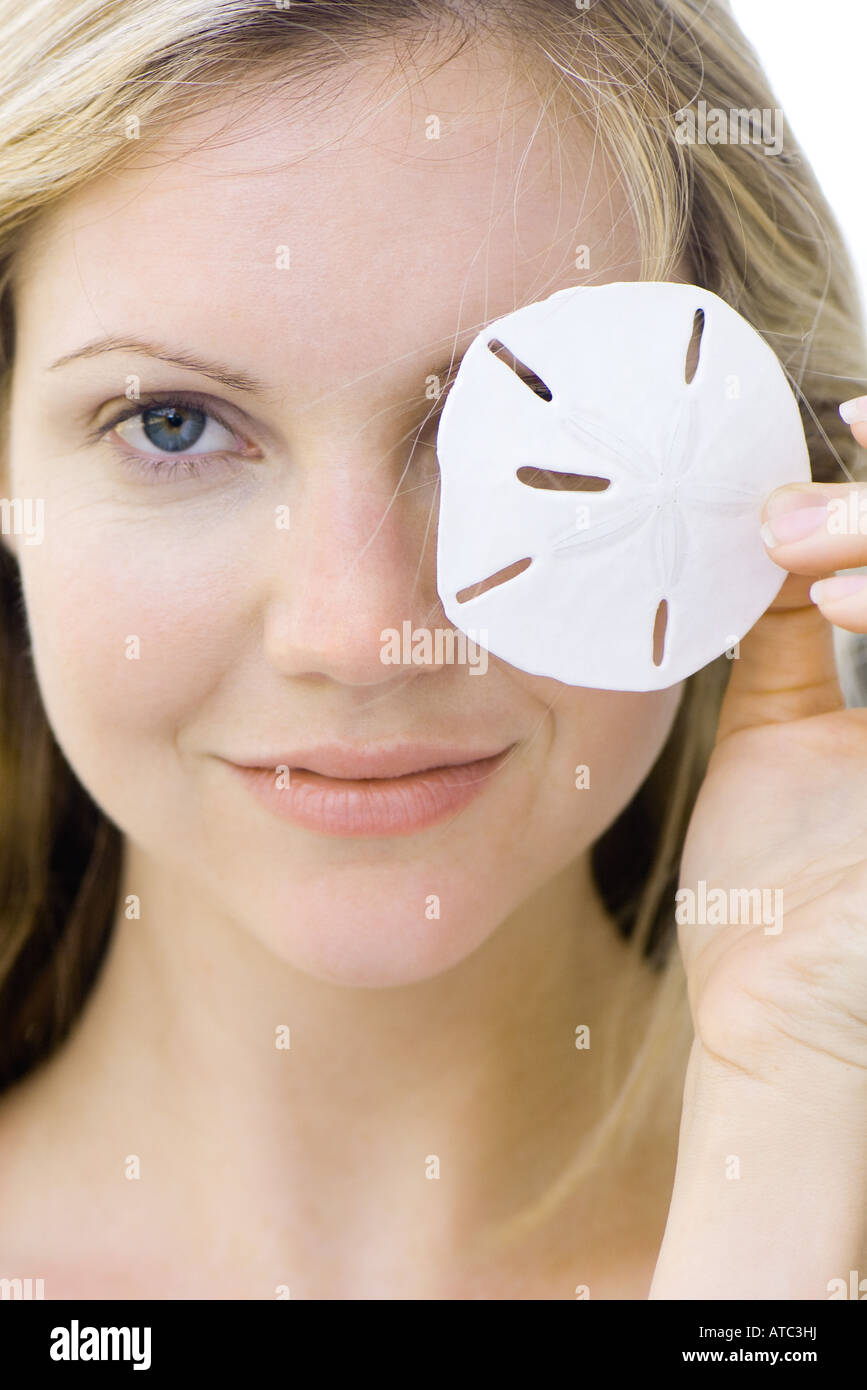 Woman covering one eye with sand dollar, smiling at camera, portrait Stock Photo
