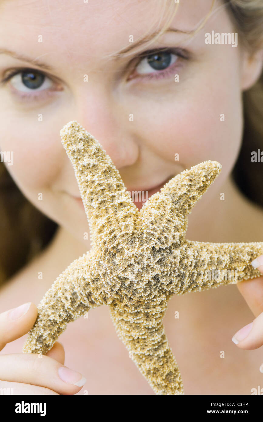 Young woman holding up starfish, smiling at camera, focus on foreground Stock Photo