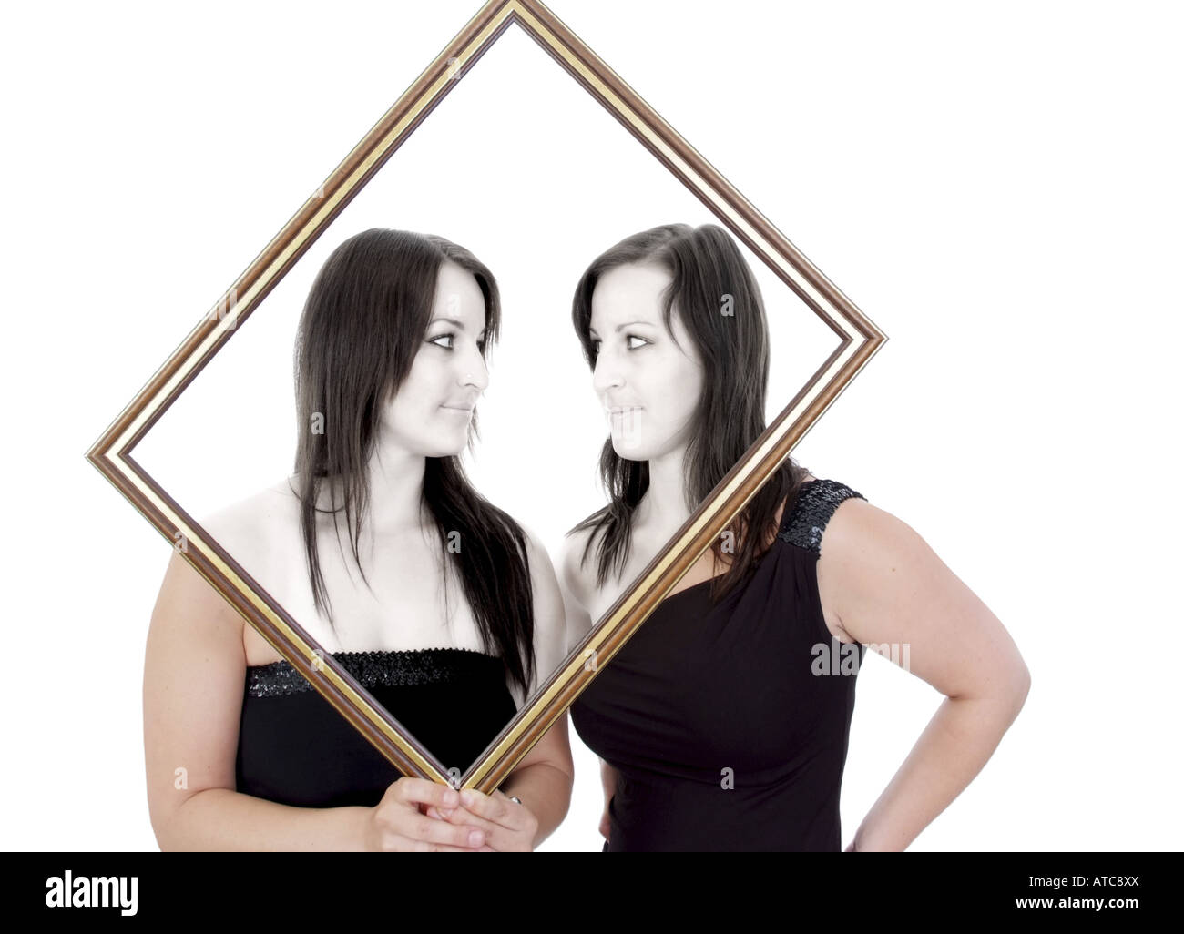 twin sisters with a picture frame, looking at one another Stock Photo