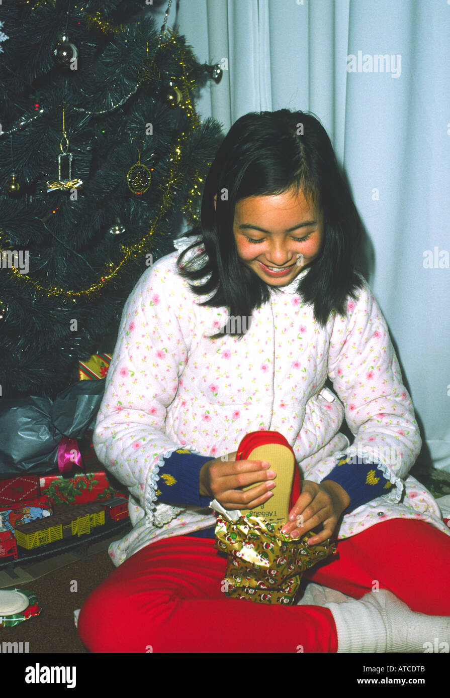 ten 10 year old girl opens presents Christmas morning next to artificial tree Stock Photo