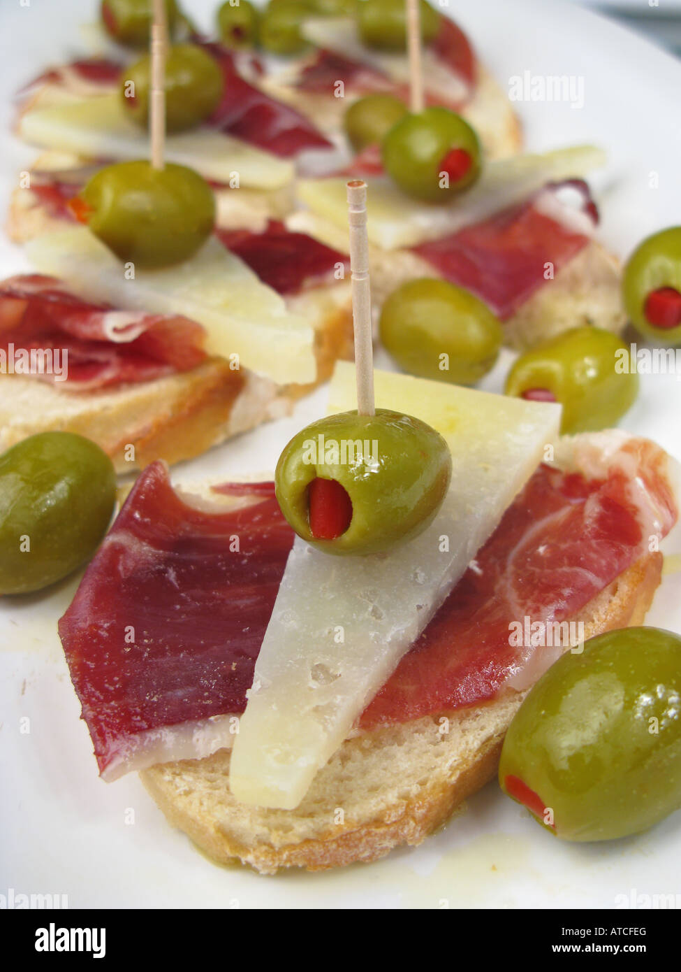 Spanish style tapa of sliced Jamon Iberico de Bellota and Manchego cheese with pepper stuffed olives on crusty stonebaked bread. Stock Photo