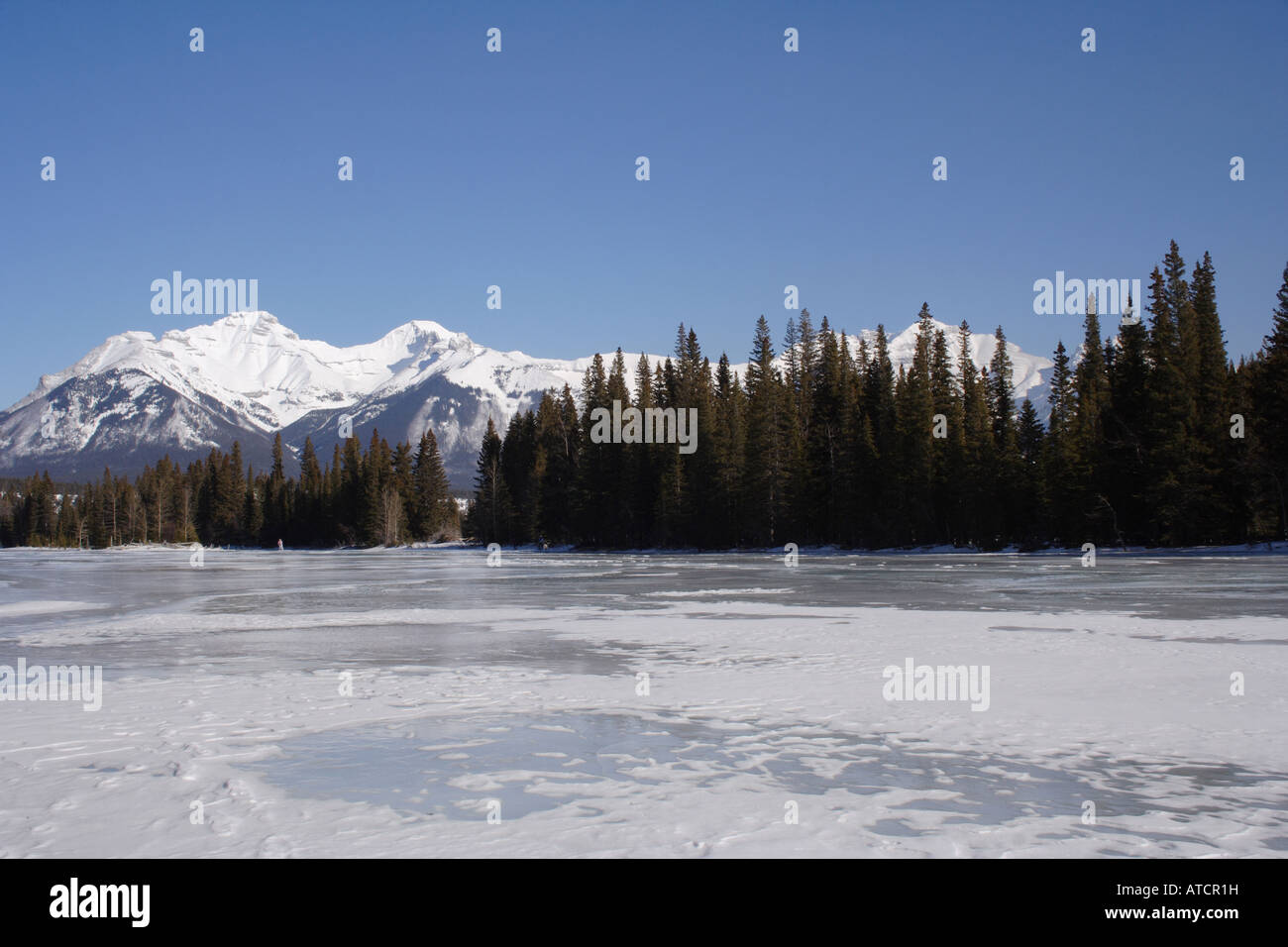 Frozen Bow river and peaks of the Rockies near Banff village, Alberta Stock Photo