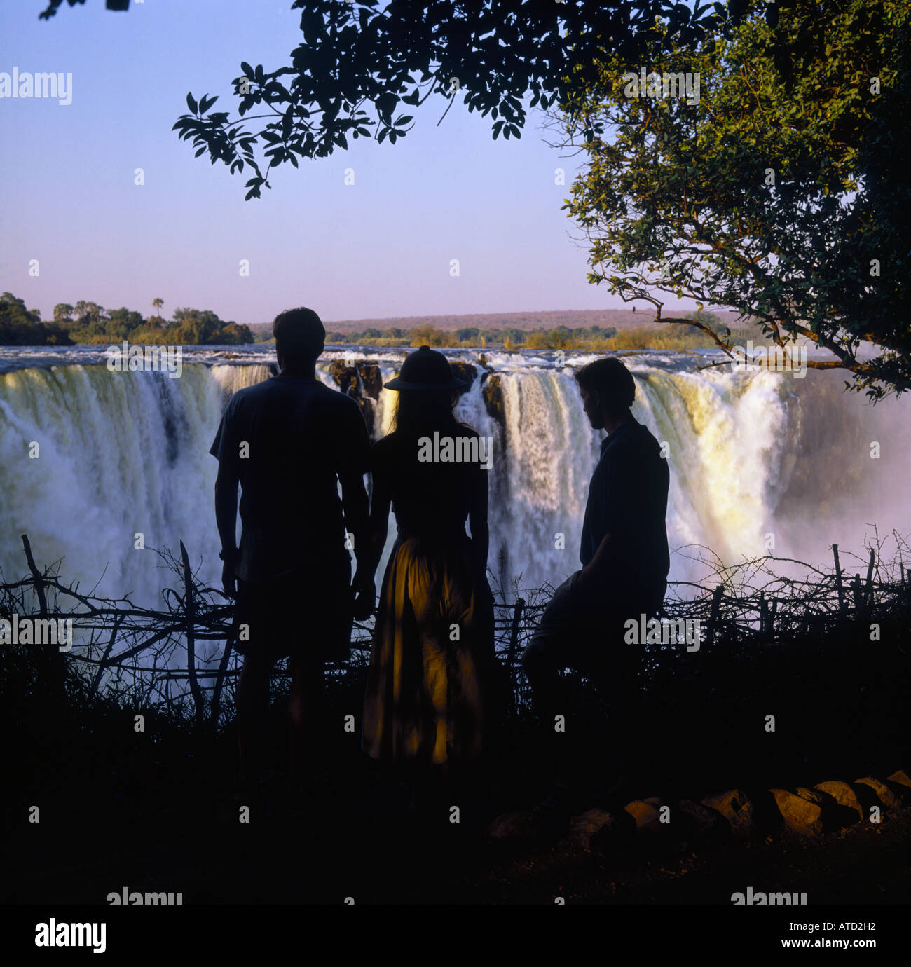 Back view of three people in silhouette looking at Victoria Falls in Matabeleland Province Zimbabwe Africa Stock Photo