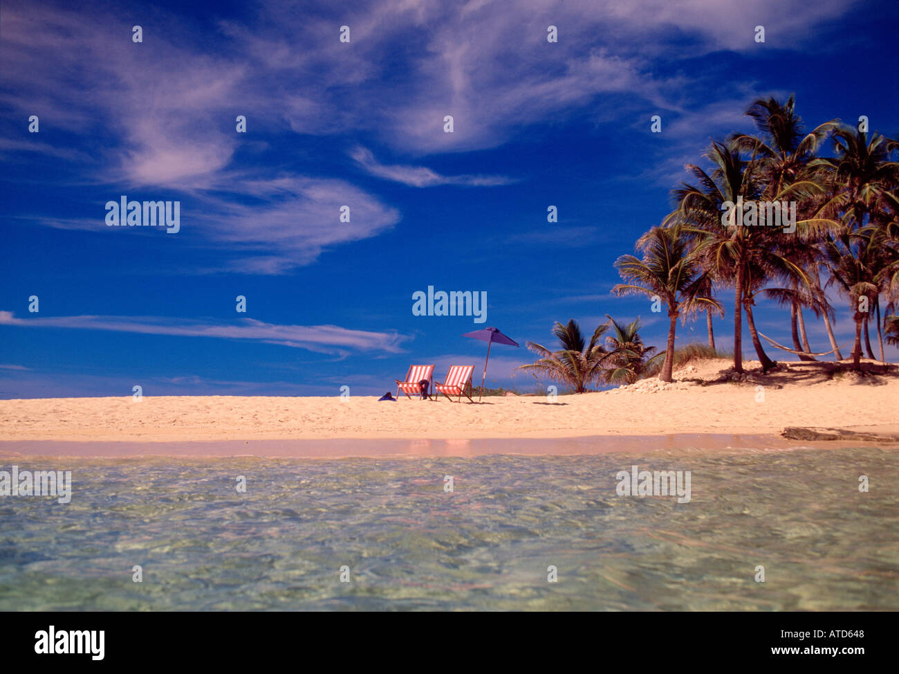 Two beach chairs and an umbrella sit on a Caribbean beach in the Bahamas Stock Photo