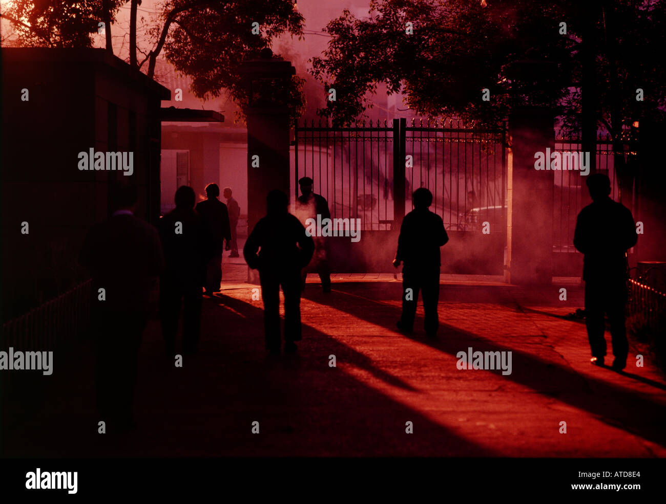 Chinese people are silhoutted against a red sky as they leave a park in the early morning in the city of Nanning Stock Photo