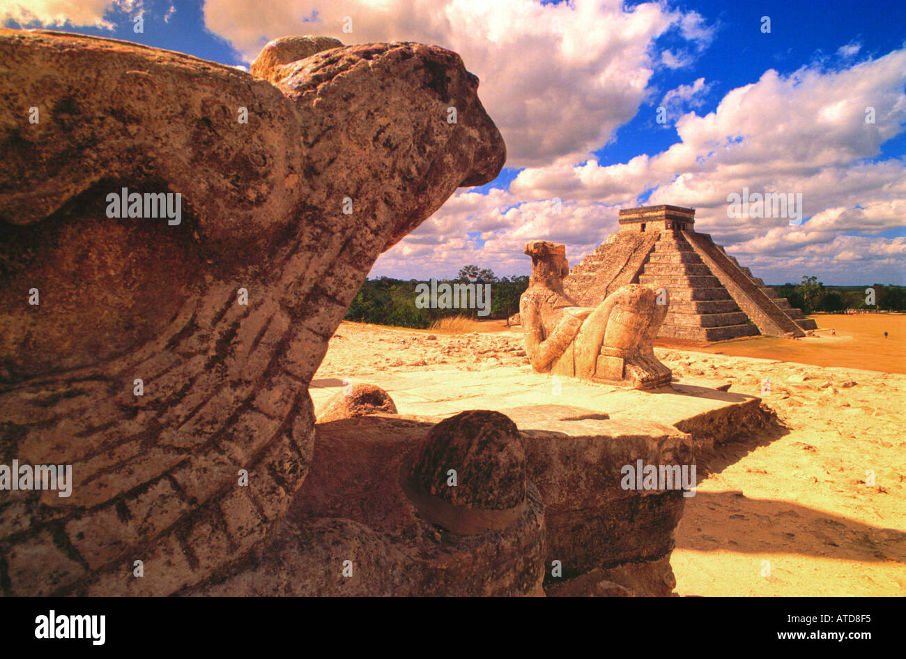 Statues of gods and reptiles sit upon the ruins of Chichen Itza with a view of El Castillo or the Pyramid in the distance Stock Photo