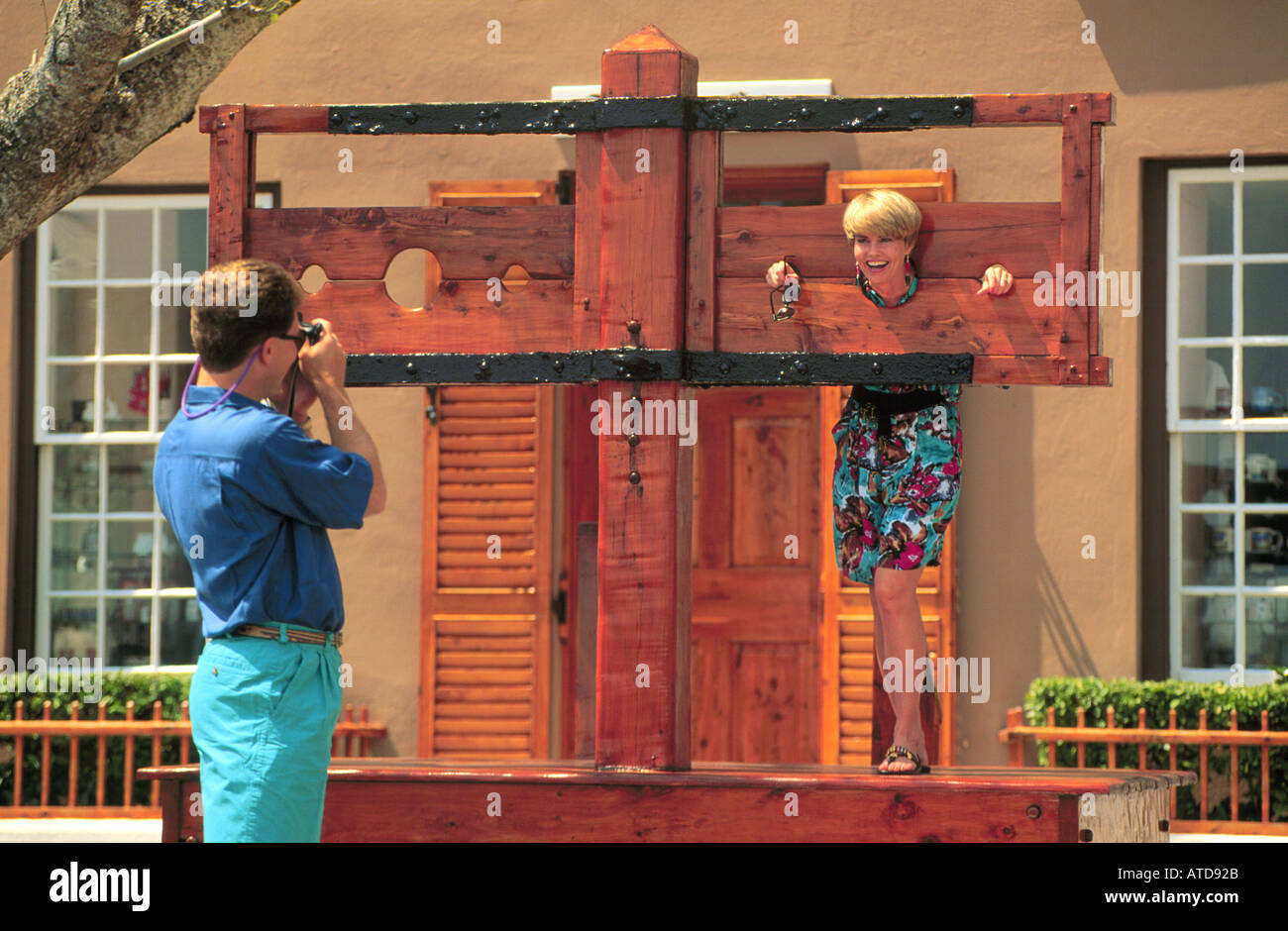 A man takes a picture or a woman playfully trapped in a wooden stockade in St Georges Bermuda Stock Photo