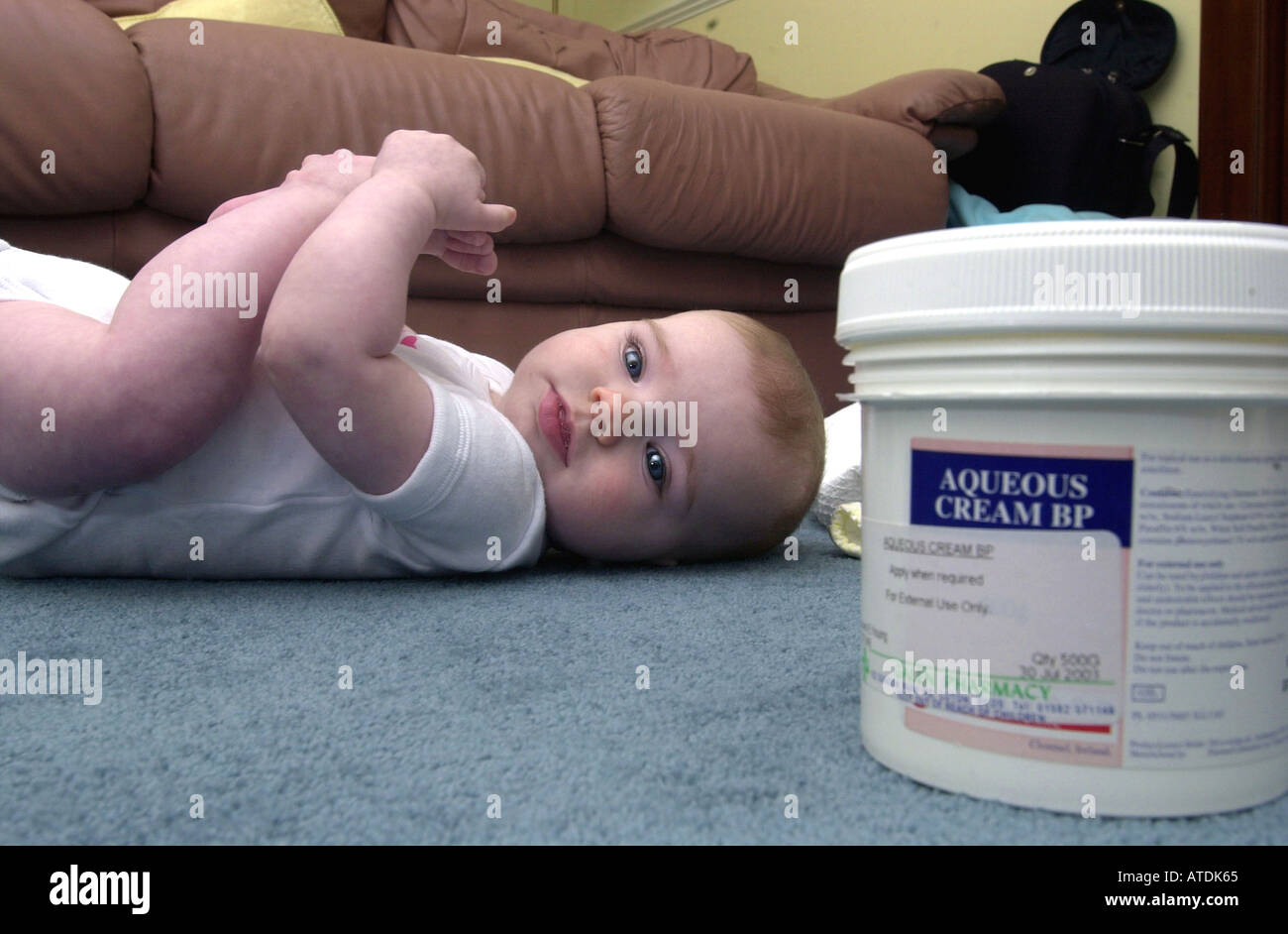 Baby lies on a carpet with some aqueous cream in the foreground UK Stock Photo