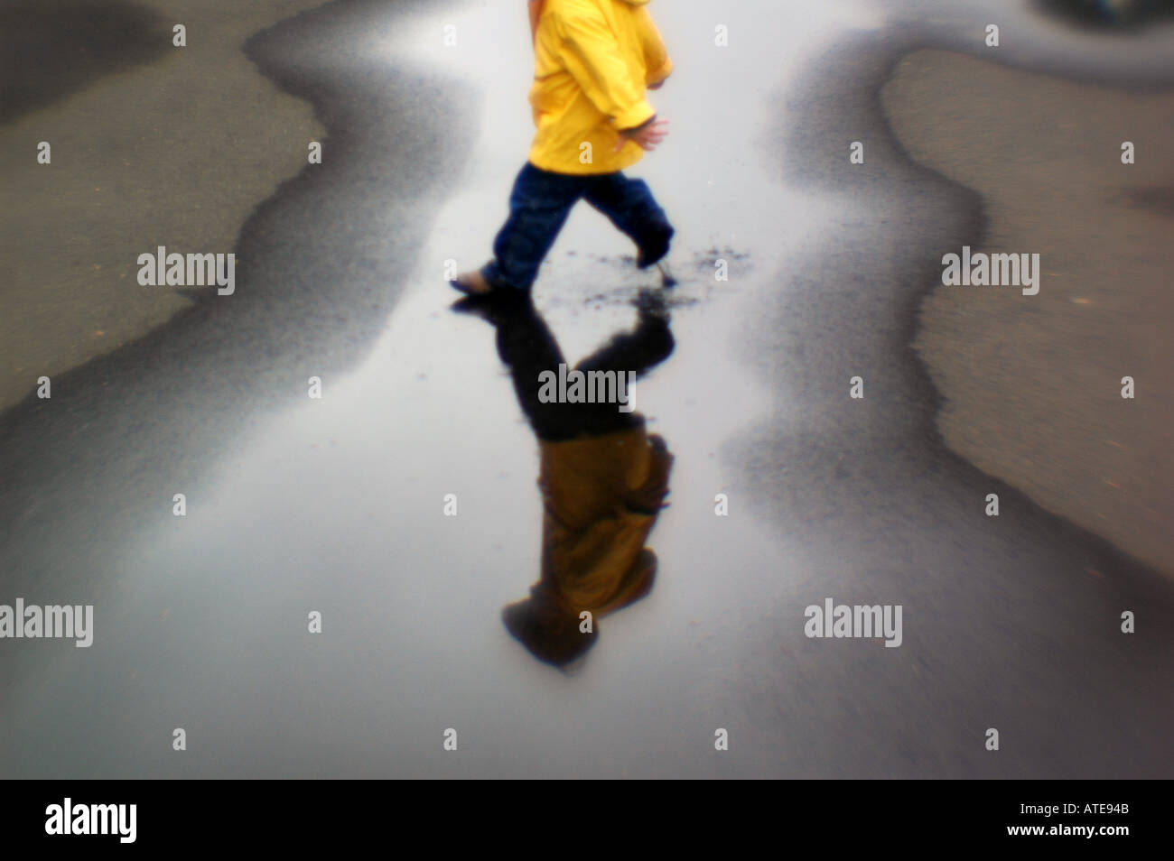 Small boy yellow jacket playing in puddle of water Stock Photo