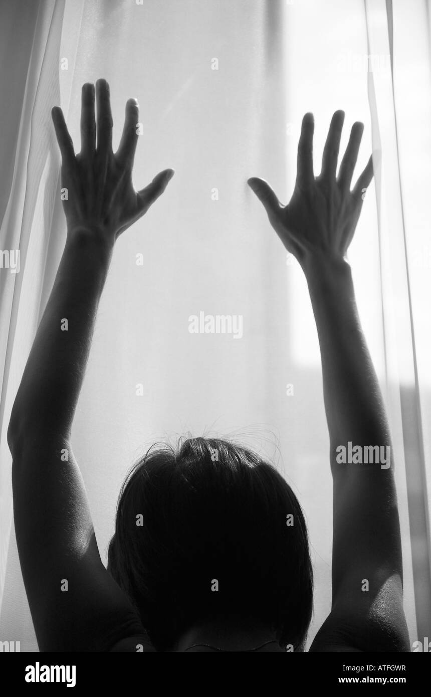 Woman silhouetted against window light placing hands on window Stock Photo