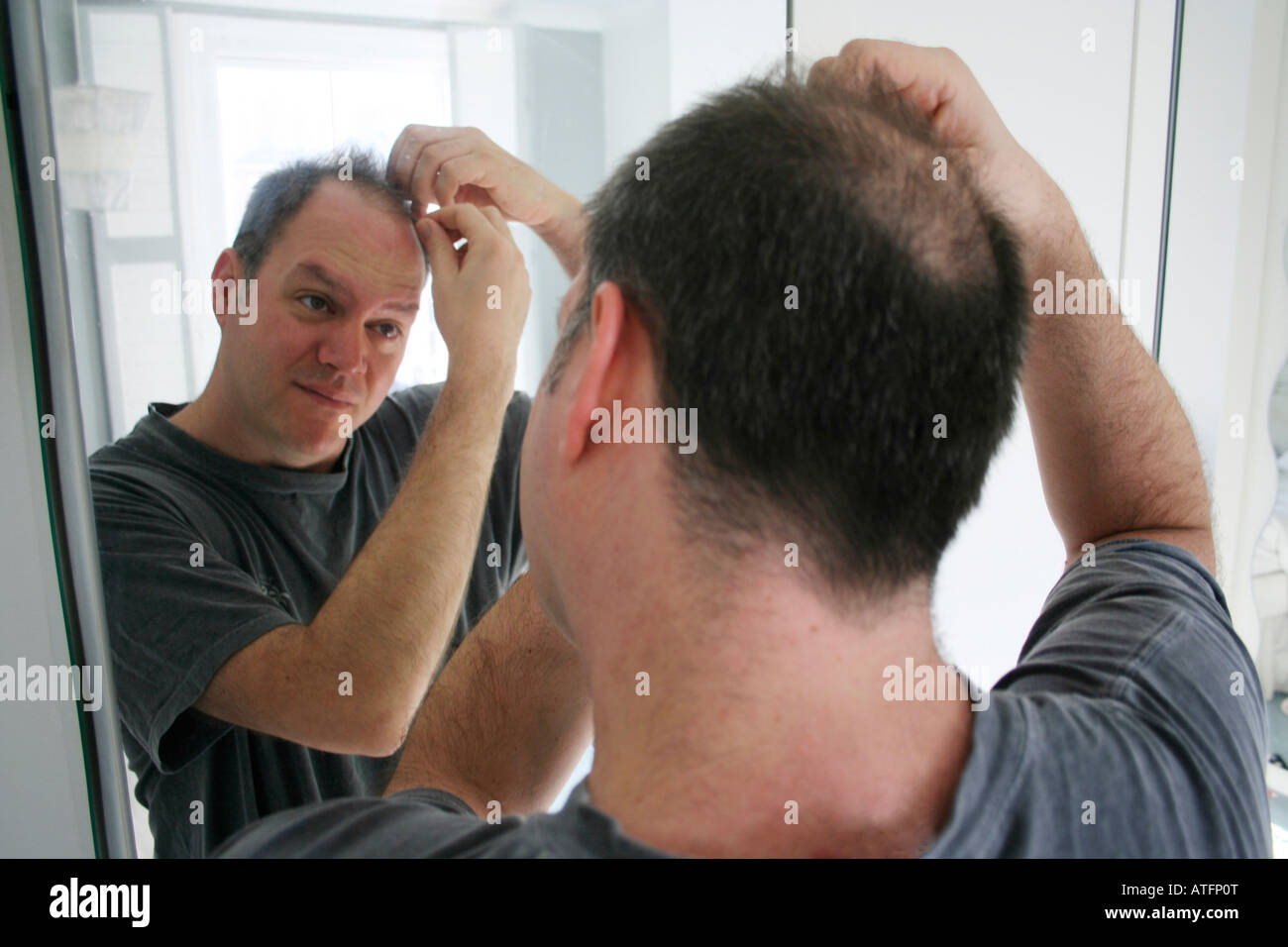 man checking bald patch in mirror Stock Photo