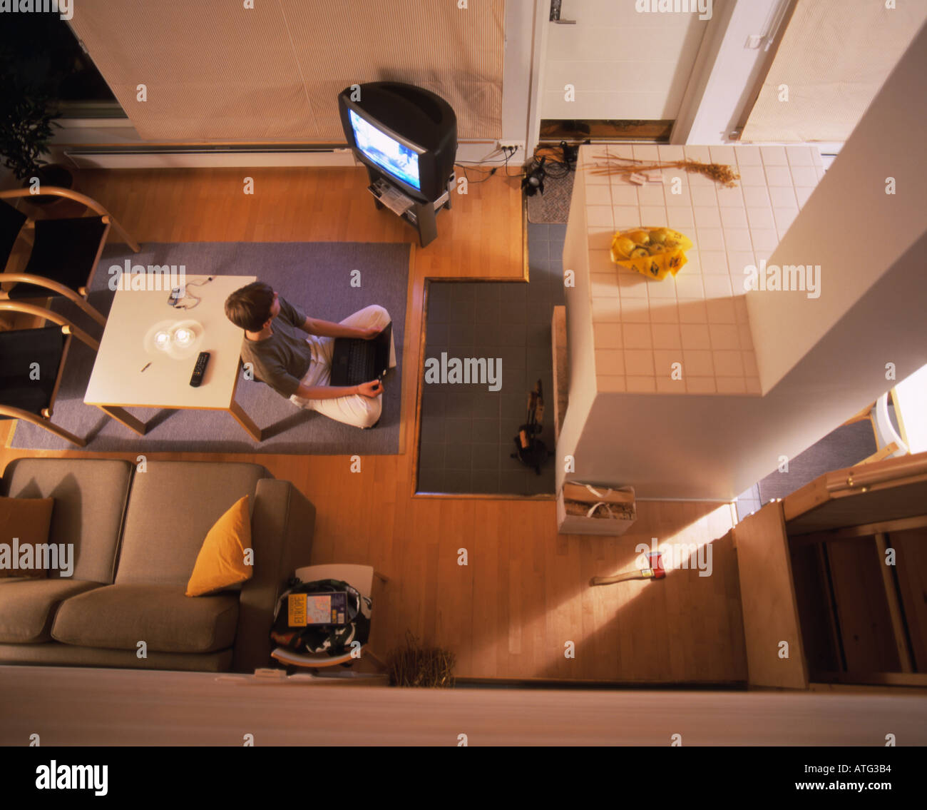 Young man sitting in a double-height / two-storey room with TV and laptop near fireplace Stock Photo