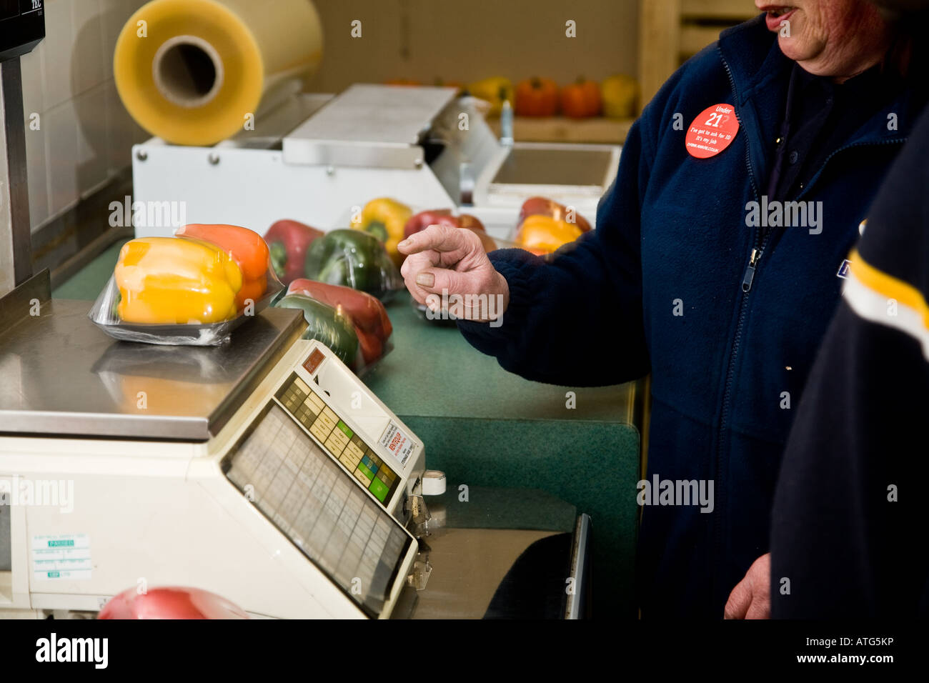 Shop assistants weighing out and pricing and packaging vegetables to go on the supermarket shelf Stock Photo