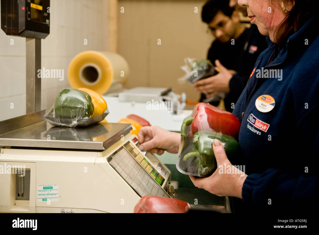 Shop assistants weighing out and pricing and packaging vegetables to go on the supermarket shelf Stock Photo