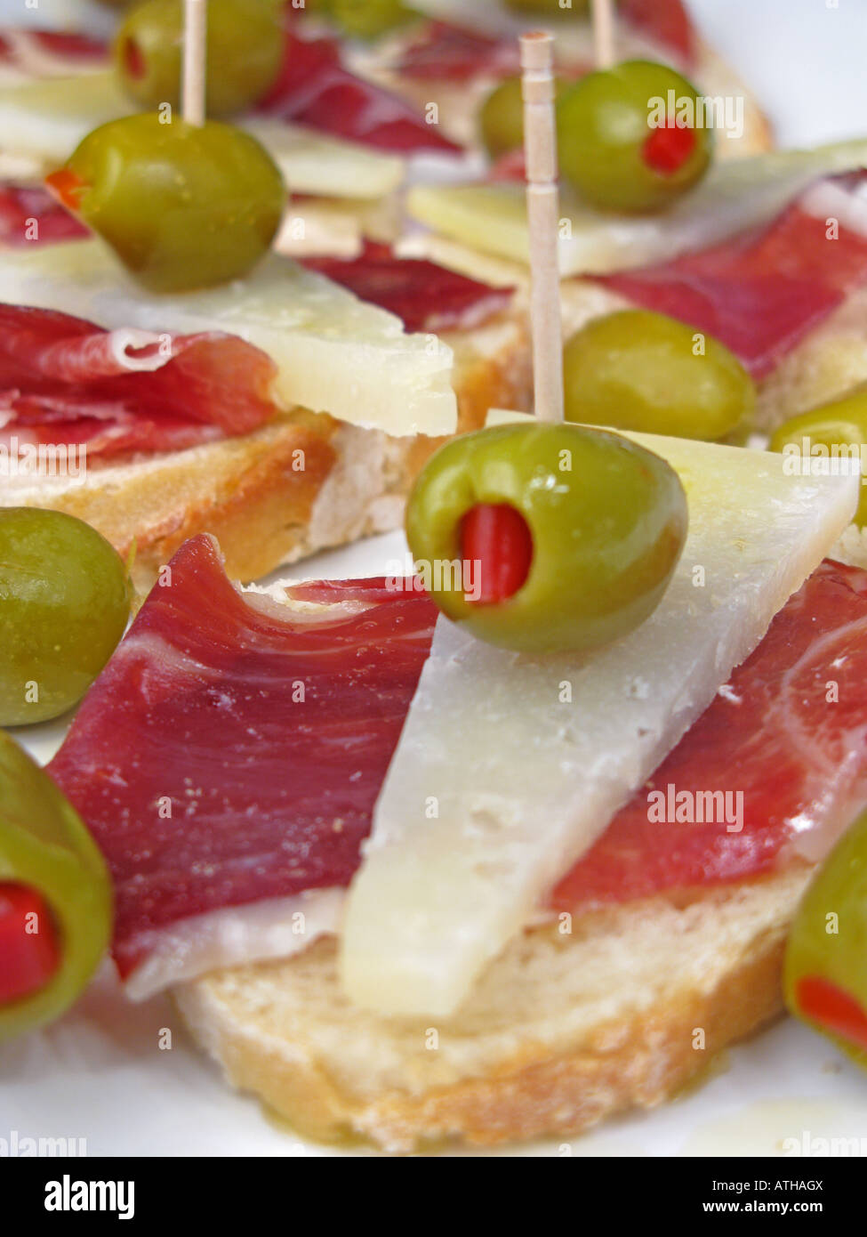 Spanish style tapa of sliced Jamon Iberico de Bellota and Manchego cheese with pepper stuffed olives on crusty stonebaked bread. Stock Photo