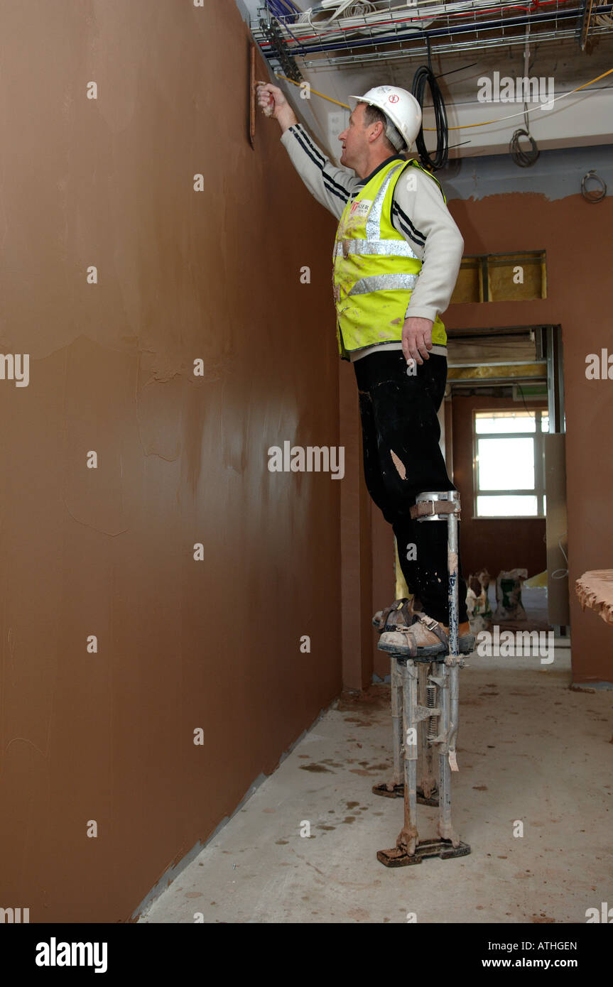 workman plastering wall using stilts to reach the top Stock Photo Alamy