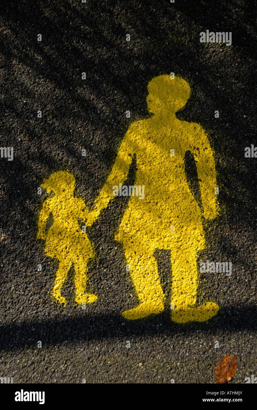 a painted yellow sign on a wet road of a child holding her mothers hand. Stock Photo