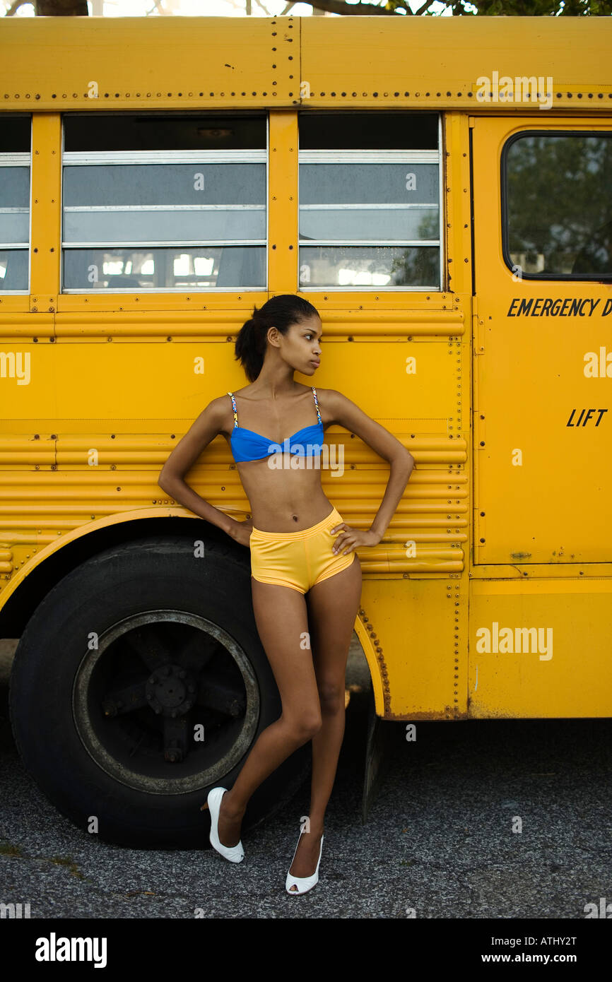 Young woman stands in fornt of a yellow school bus parked in Coney Island Stock Photo