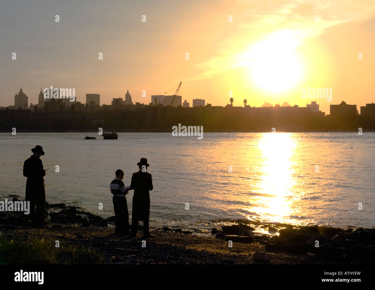 Orthodox Jewish family preying at sunset by east river Stock Photo