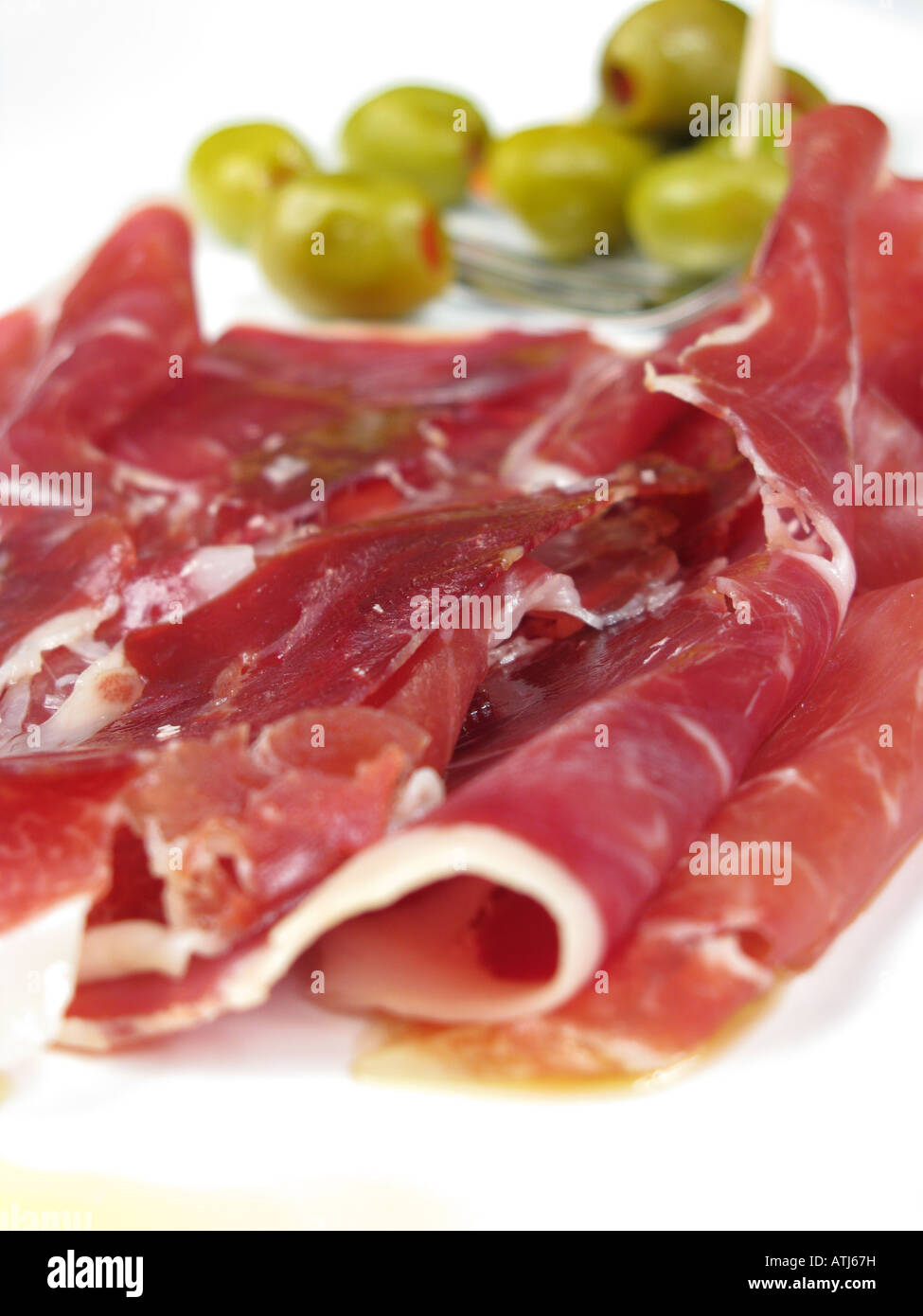 A Spanish-style tapa of thinly-sliced Jamon Iberico de Bellota, with pepper-stuffed olives behind. 2008. Stock Photo