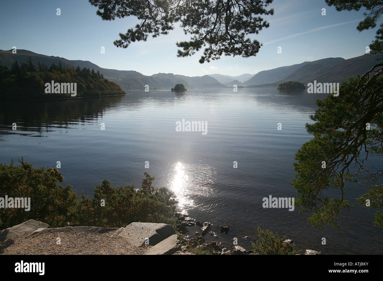 Trees water lake sun reflections ' overhanging sun trees'rockery 'islands in lake' mountains hills Stock Photo