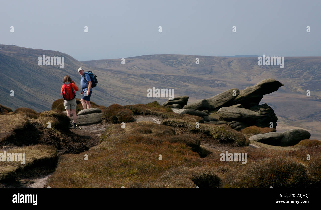 Two walkers passing gritstone outcrop on Kinder Scout, near Edale, Peak National Park, Derbyshire UK Stock Photo
