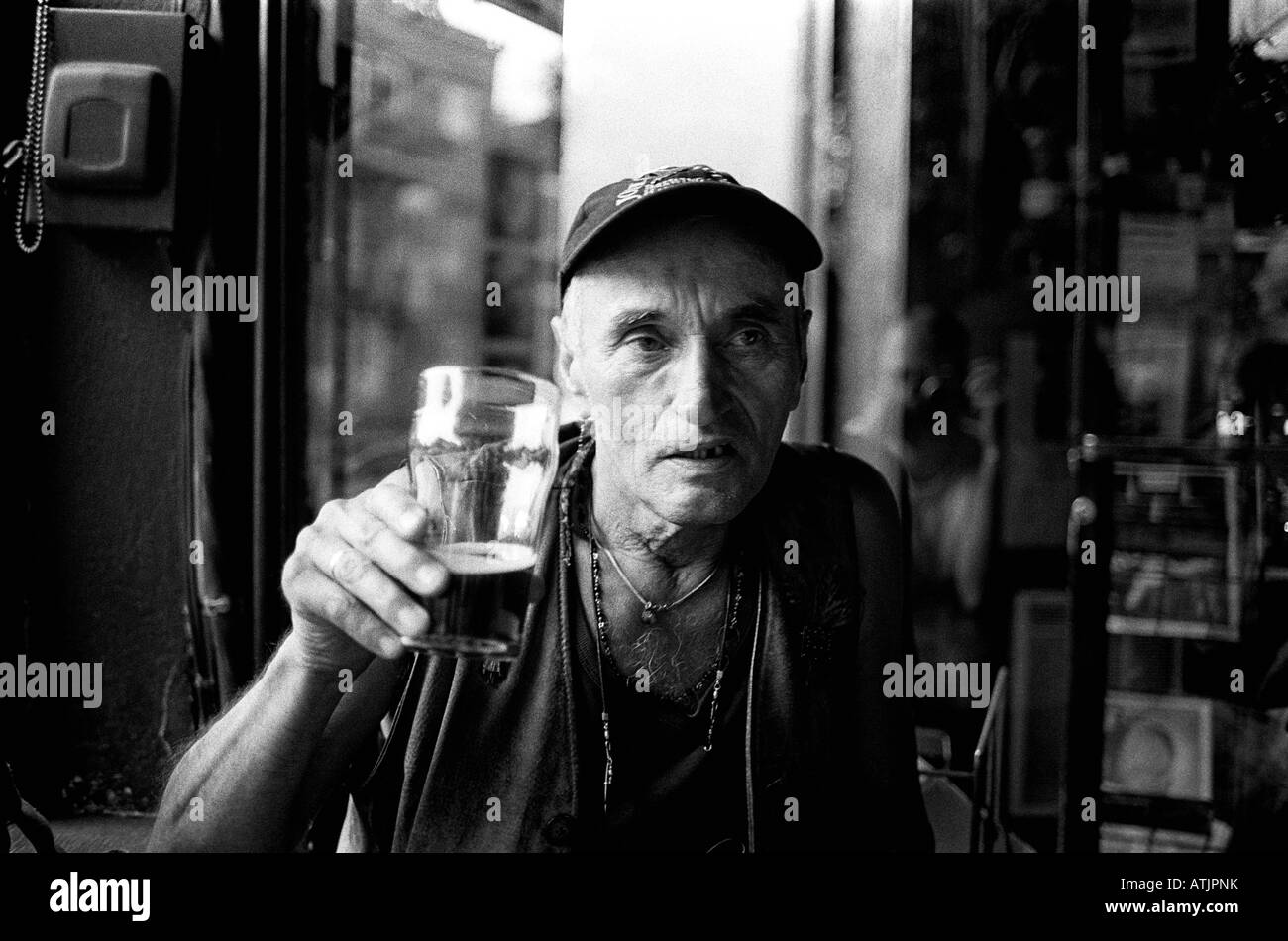 Elderly man in pub holds beer as if to toast viewer. Stock Photo